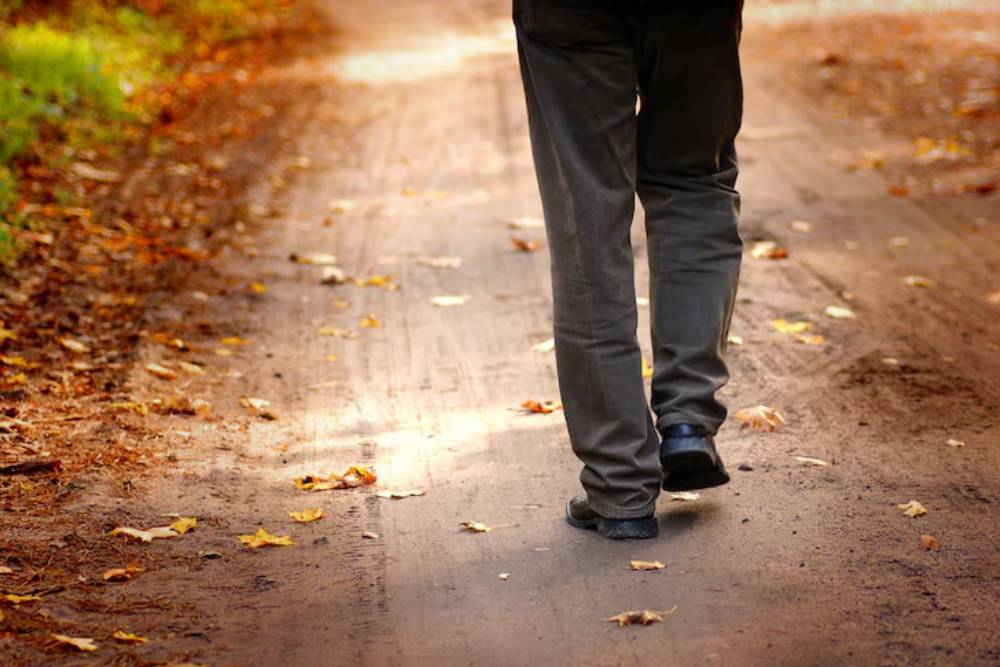 A person walks alone down a peaceful path surrounded by fallen leaves, representing personal growth through an addiction aftercare program Columbus OH.